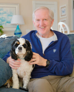 bill slater seated on couch holding his dog on the left side